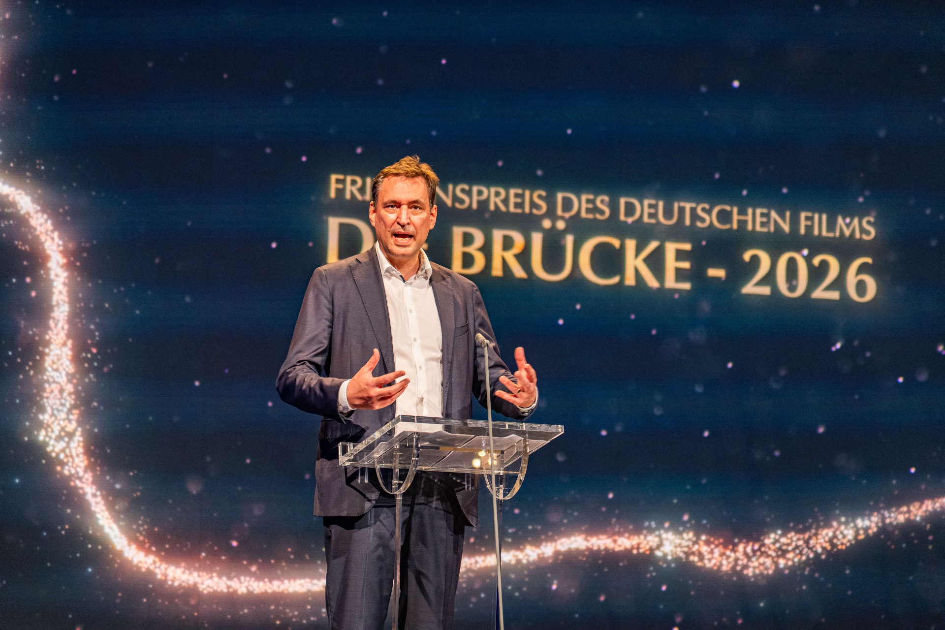 Ansprache auf der Bühne vor dem Schriftzug Die Brücke 2026